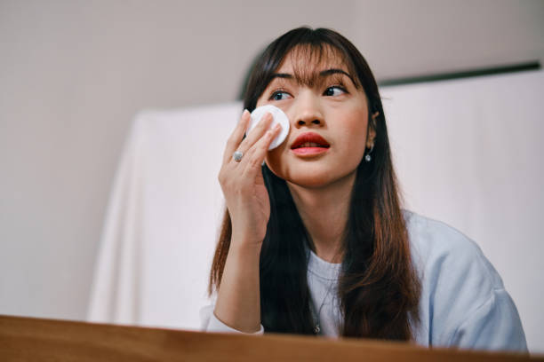 bella donna asiatica che rimuove l'applicazione del trucco davanti allo specchio - detergente per il viso foto e immagini stock