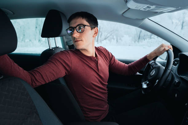 眼鏡をかけた運転手は、車が逆転している間、より良い視界のために引き返しました。駐車場と運転訓練のコンセプト - 逆進 ストックフォトと画像