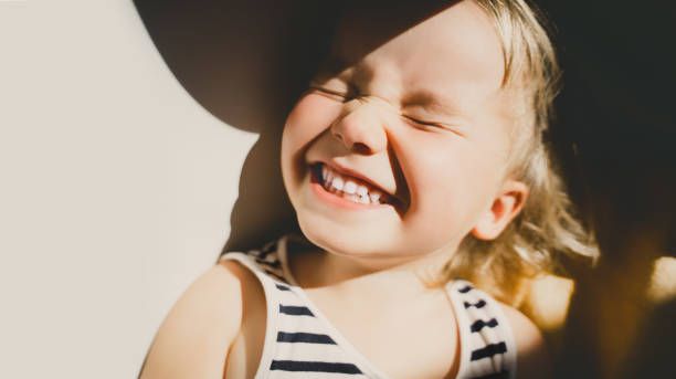 süßes kleines mädchen lächelnd und schielend im sonnenlicht. glückliches kleinkind mit spaß. porträt des verspielten vorschulalters. lifestyle-fotografie. - laughing children stock-fotos und bilder