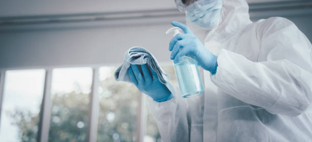 Man in virus protective suite and mask using alcohol cleaning covid19 infected area, Virus disinfection concept stock photo