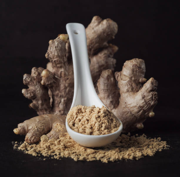 istock Ginger root and ginger powder in a spoon on black background, close up. 1302078209