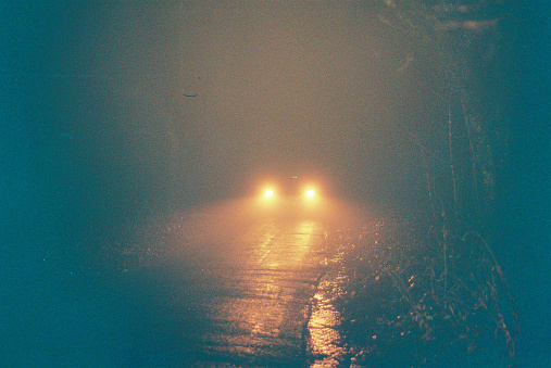 Rain and mist as a car drives down a wooded country lane, 35mm Lomography Redscale film.