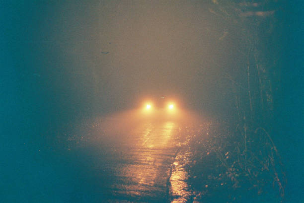Car at night on country lane Rain and mist as a car drives down a wooded country lane, 35mm Lomography Redscale film. analog photos stock pictures, royalty-free photos & images