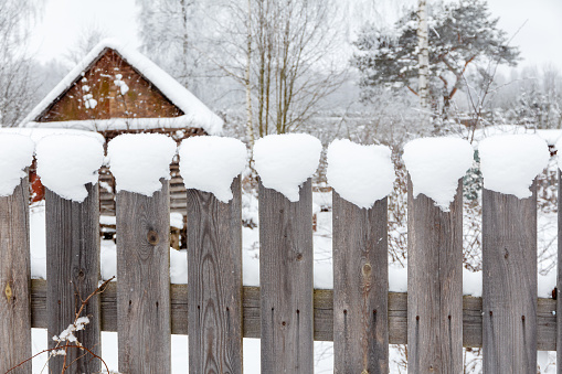 Wooden rural fence covered with snow. Snowy winter rural landscape