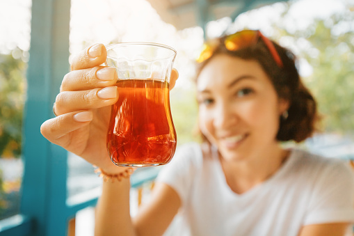 Happy middle Eastern woman drinks traditional Turkish tea on the veranda or terrace of an outdoor restaurant