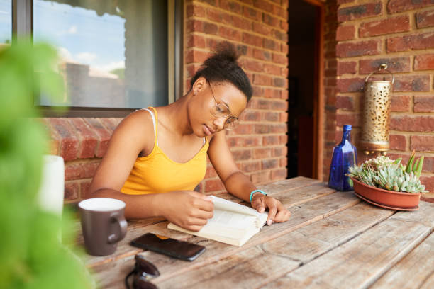 istock Young woman reading a book outside at a patio table 1302086963