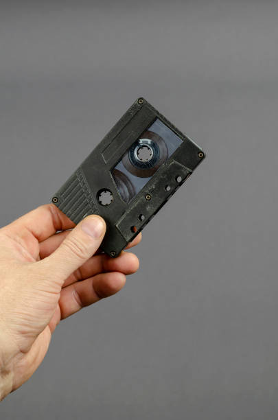 istock Handholds an audio cassette on a gray background. 1302089879