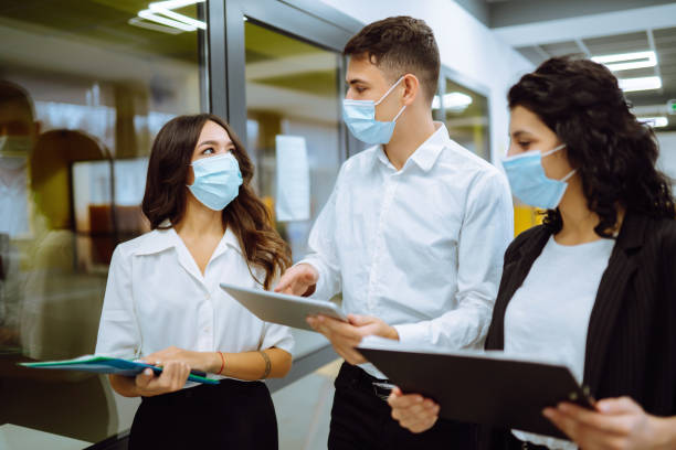 istock Three business colleagues in protective face mask discussing work related matters on an office building hallway 1302091492