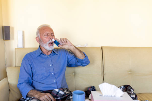 istock An Older Sick Man is Lying in his Bed Covered with a Blanket and Using Nasal Spray. 1302092413