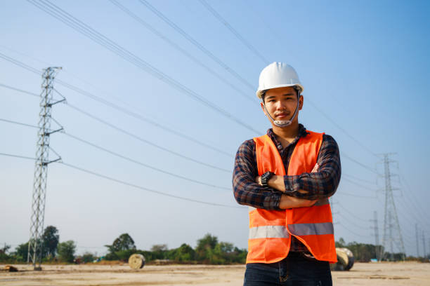 istock Portrait of Electrical Engineer, field engineer, foreman, owner standing in construction site project and Electric power line and pole in background. Asian engineer. High voltage power line pylon. 1302093558