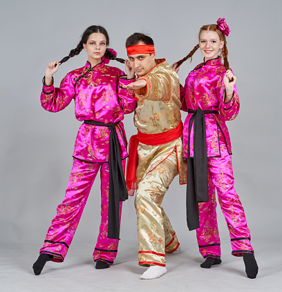 Three dancers (two teenage girl and young man) are dressed in a Chinese traditional clothing. The dancers are dancing Chinese folk dance and showing traditional poses. They are smiling looking at the camera. Studio shooting