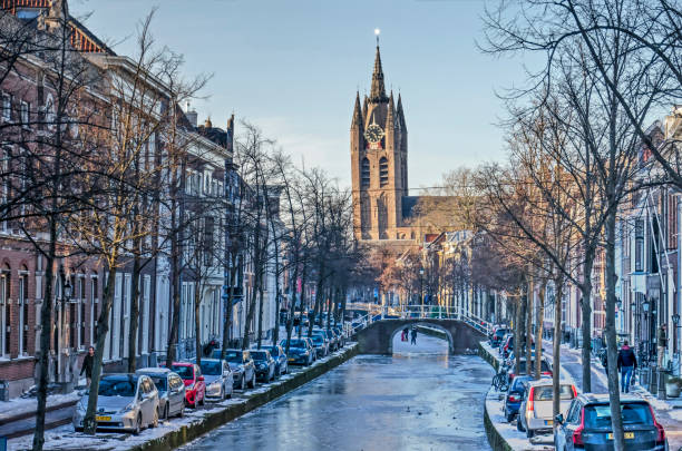 Delft canal and church Delft, The Netherlands, February 13, 2021: view along frozen Oude Delft canal towards the leaning tower of the Old Church delft winter netherlands snow stock pictures, royalty-free photos & images