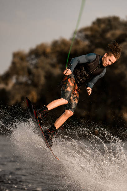 istock Athletic muscular guy skillfully jumps on wakeboard holding rope in his hand. 1302100886