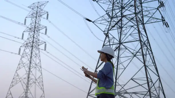 Photo of Female electrical engineer working near to High voltage tower.