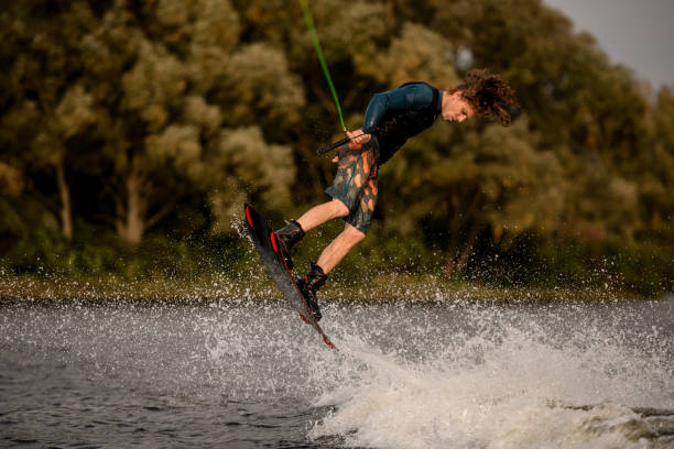 istock young man holds rope in his hand and skillfully jumping on wakeboard. 1302104519