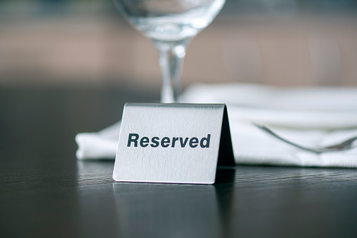 Reserved iron sign on wooden table in front of white tablecloth and wine glass at a cafe or restaurant