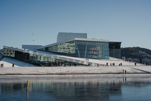 February 13-2021. Oslo, Norway:  The modern architecture of the Oslo Opera House in Oslo, Norway. Tourists walk on the marbled paving that surrounds the opera house.