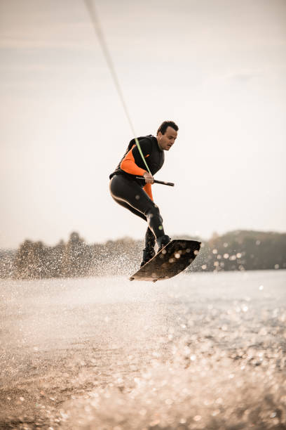 istock guy in wetsuit having fun and jumping on the wave on wakeboard. 1302106049