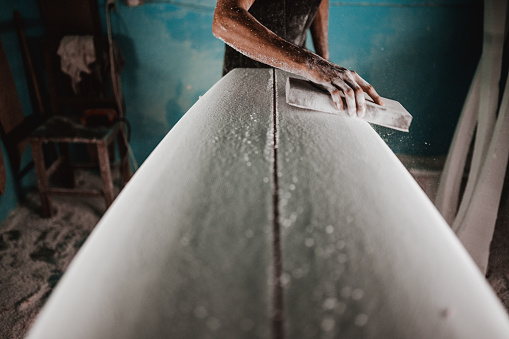Craftsman hand shaping a surfboard blank, working on the bottom of the board