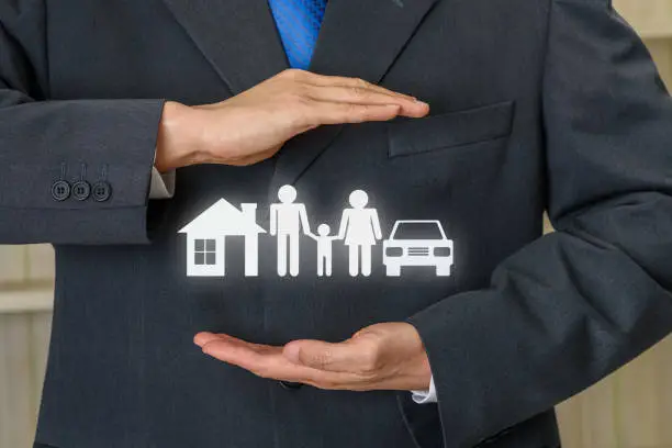 Photo of Broker or insurer uses both hands to protect parents e.g. father, mother, child, a house and sedan car