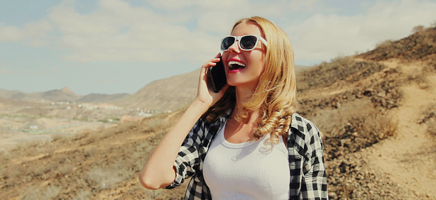 Portrait of happy young laughing woman calling on a phone on a hiking trail on top of the mountain, Tenerife, Canary Islands, Spain