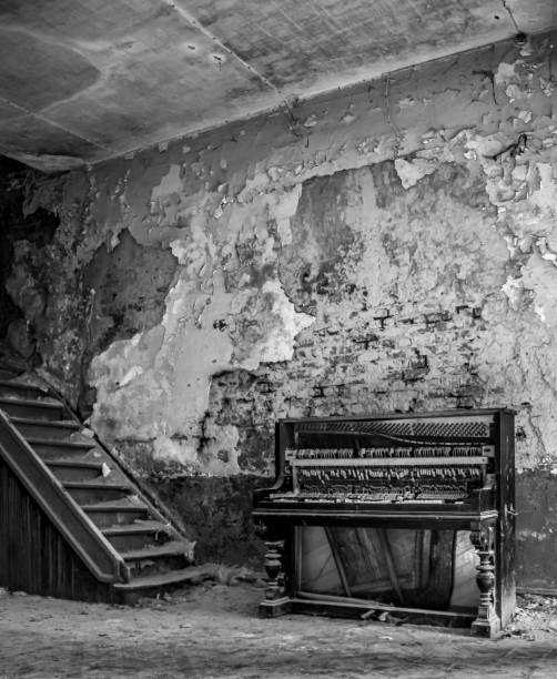 Piano by a staircase in an old decayed room, in monochrome
