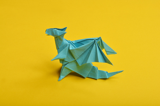 Blue origami paper dragon on yellow background