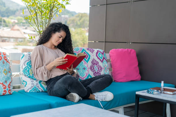 istock Young woman reading a book sitting on a terrace 1302120160