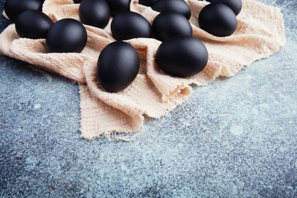 istock Black Easter eggs on a linen napkin on a blue texture table. Easter celebration concept. View from above. 1302122639