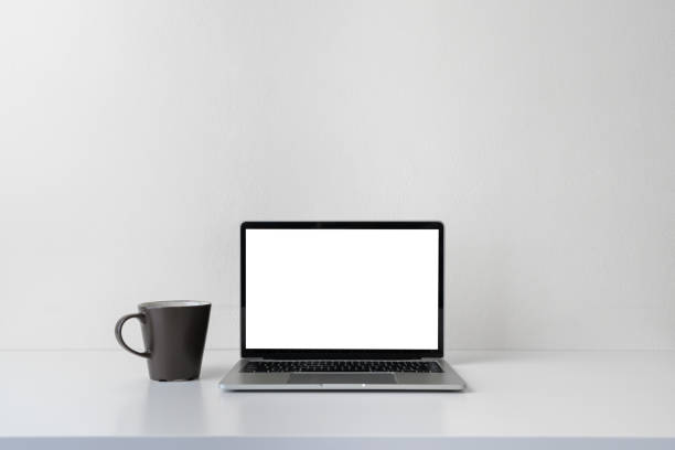 istock Modern contemporary workspace with blank screen laptop computer and coffee cup on office desk table on white background for copy space. Home office workplace concept. 1302123356