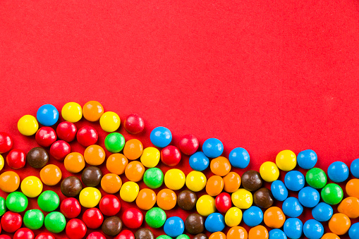 M&M's candy on the red background, colorful candy and multicolored gradient