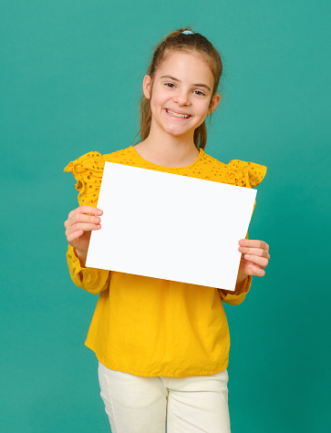 1 white teenage girl 10 years old in a yellow blouse holding a white sign and smiling on a green background