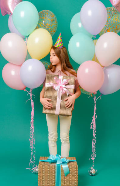 1 ragazza bianca di 10 anni con un regalo, palloncini rosa, gialli, blu per una vacanza su sfondo verde - 10 11 years cheerful happiness fun foto e immagini stock