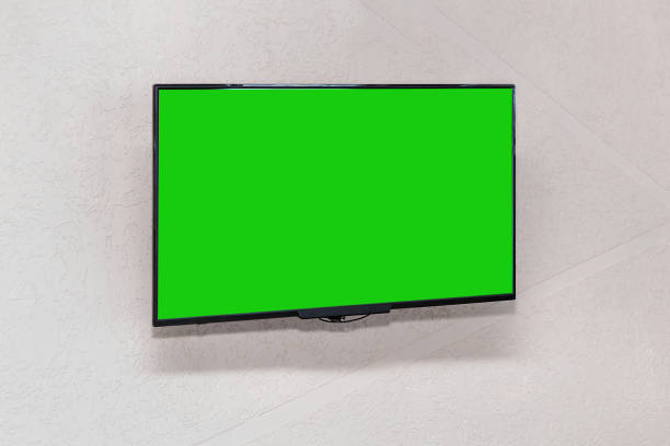 istock Modern TV lcd panel in black frame with blank green mockup screen hangs on white wall 1302130257