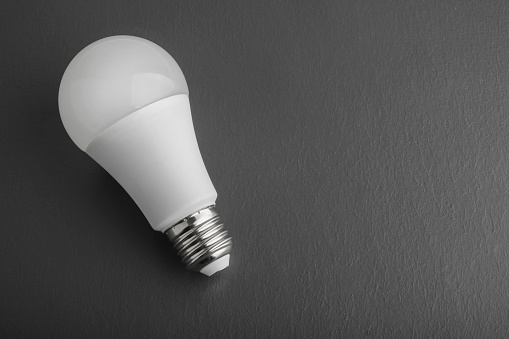 White energy saving LED light bulb on an dark grey background with copy space. LED white bulb, concept of new idea