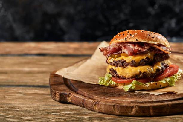 el concepto de comida rápida americana. una jugosa hamburguesa americana con dos empanadas de ternera y una cerveza oscura sobre una mesa de cristal sobre fondo de madera. copiar espacio - jugoso fotografías e imágenes de stock