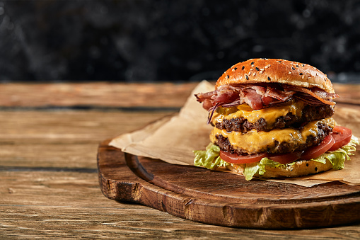 The concept of American fast food. A juicy American burger with two beef patties and a dark beer on wooden background. Copy space.