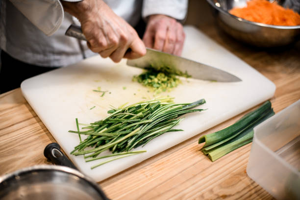 Chopped spring onions in the foreground on a wooden chopping board with full spring onions in the background