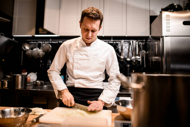 view of male chef in white jacket chops onion in kitchen