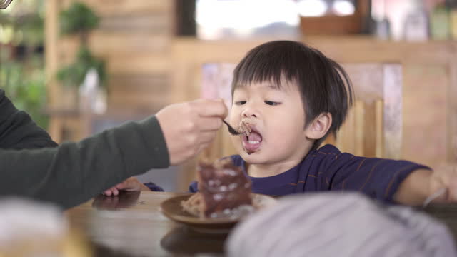 Asian Mother and Baby boy eating Chocolate cake in a cake shop