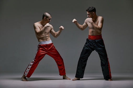 Boxers athletic guys fighting on gray studio background during kickboxing workout, mixed fight concept. High quality photo