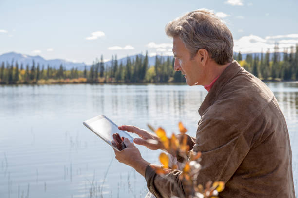 istock Man using tablet relaxes by alpine lake in the morning 1302145726