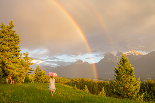 She looks off towards rainbow forming over Canadian Rockies in the distance