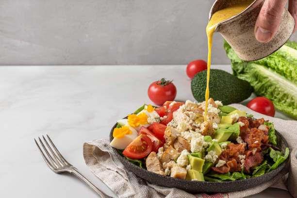 un condimento per insalata versato a mano in insalata di cobb con pollo, avocado, pancetta, formaggio blu, pomodoro e uova. dieta cheto - condimento per insalata foto e immagini stock