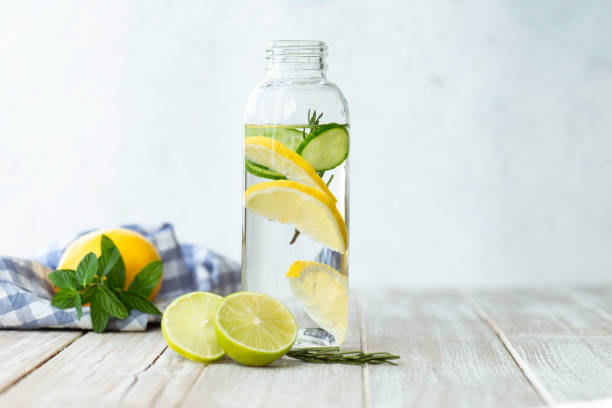Detox Bottle of infused water on white wood with a slice of lemon , cucumber and rosemary leaf in it. lemon fruit stock pictures, royalty-free photos & images