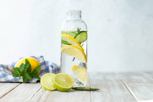 Detox Bottle of infused water on white wood with a slice of lemon , cucumber and rosemary leaf in it. infused water stock pictures, royalty-free photos & images