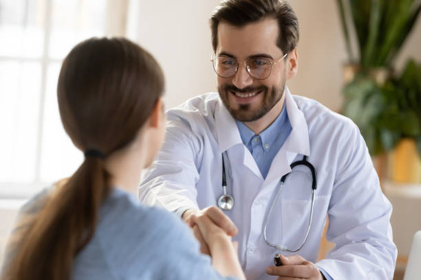 pleasant smiling male doctor meeting young woman patient at clinic - médico geral imagens e fotografias de stock