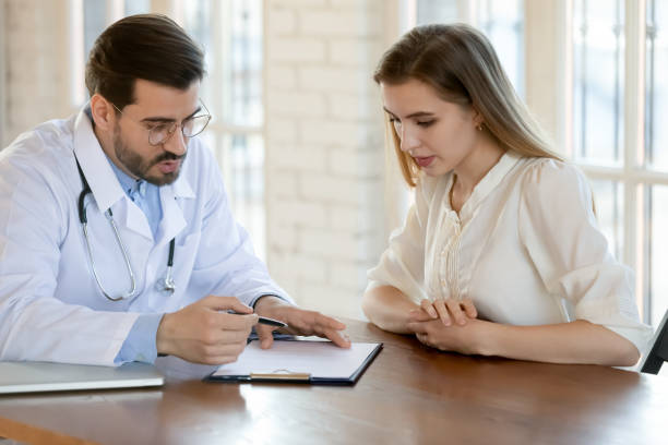 Capable qualified male doctor prescribing treatment to young female patient Doc writing prescription. Capable qualified millennial male doctor attending physician gynecologist gp consulting young female patient at hospital cabinet, ordering medication, prescribing treatment qualified report stock pictures, royalty-free photos & images