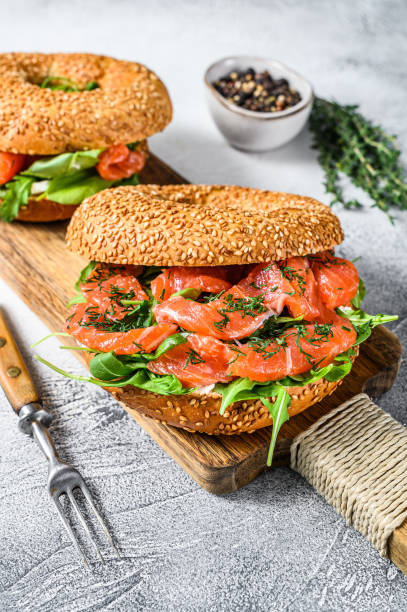 istock Smoked salmon bagels sandwich with soft cheese and arugula on a cutting board. White background. Top view 1302151134