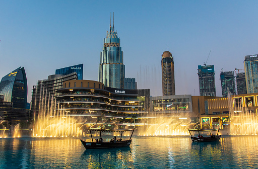 Dubai, United Arab Emirates - January 16, 2021: Dubai mall fountain show in front of Dubai mall shopping and leisure area surrounded and modern downtown buildings in the United Arab Emirates at blue hour